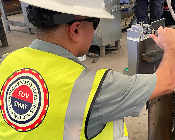 SMAT inspector in a branded hi-vis vest measuring a weld with a digital caliper